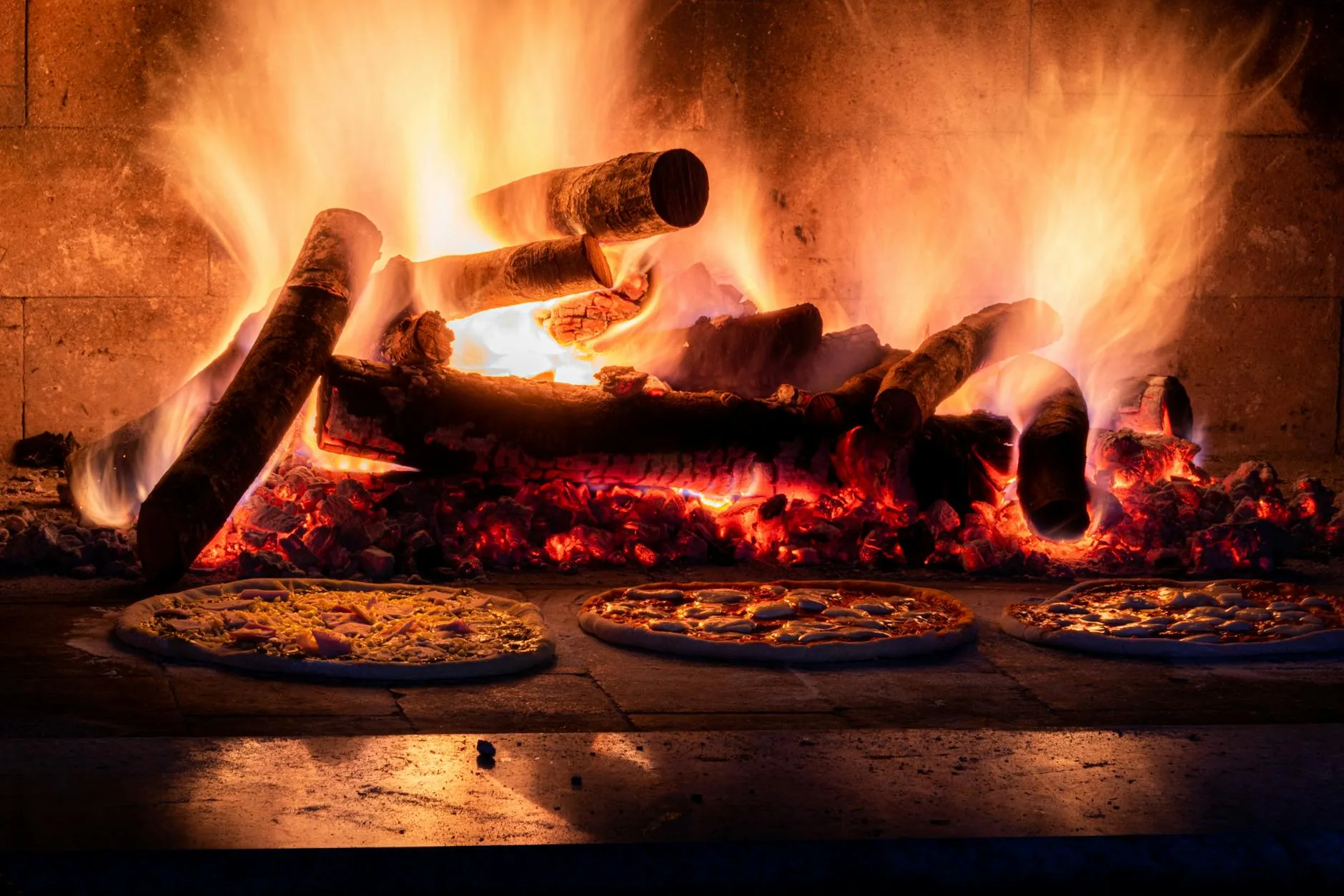 Pizza cooking inside a wood fired oven with visible flames